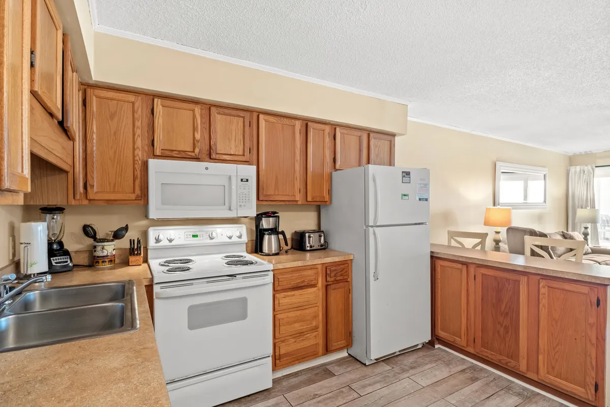 This image showcases a welcoming kitchen space featuring modern kitchen appliances, generous wooden cabinetry, and ample counter space. The room is arranged for ease of use and social gatherings, suggesting a setting where families or friends can cook and share meals together.