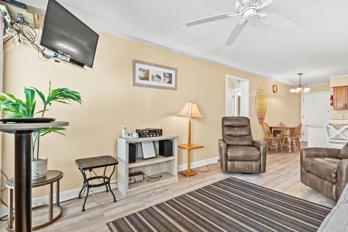 A view from the living area, featuring a comfortable recliner, a lamp, a television, an indoor plant, and a glimpse of the dining area set nearby. The arrangement emphasizes the open-plan layout, making it perfect for socializing or transitioning from relaxation to shared meals.