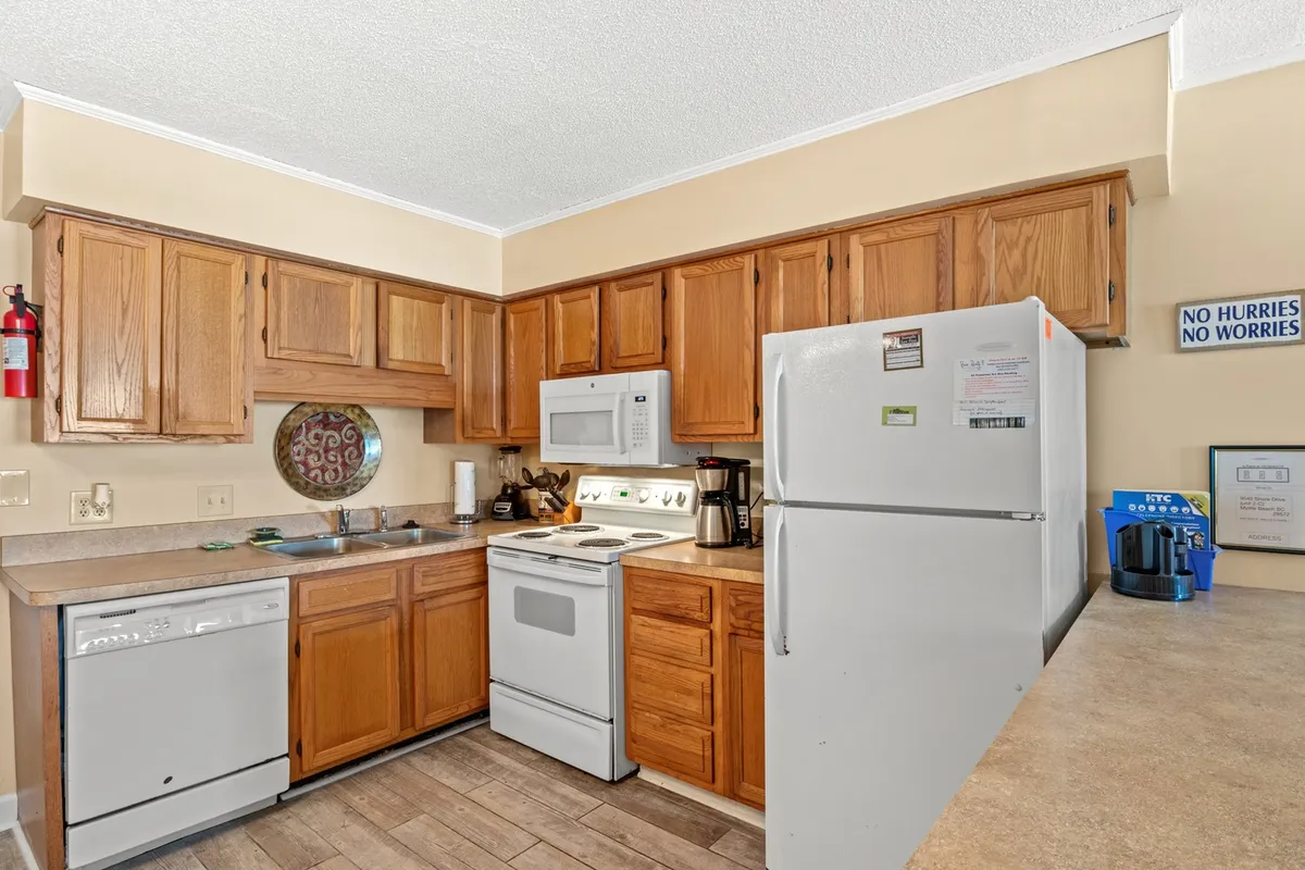 A warm, casual kitchen scene with wooden cabinets, white appliances, and a countertop coffee maker. The layout and visible tools suggest a homey, functional space ideal for both simple meal prep and special culinary moments like baking with family.