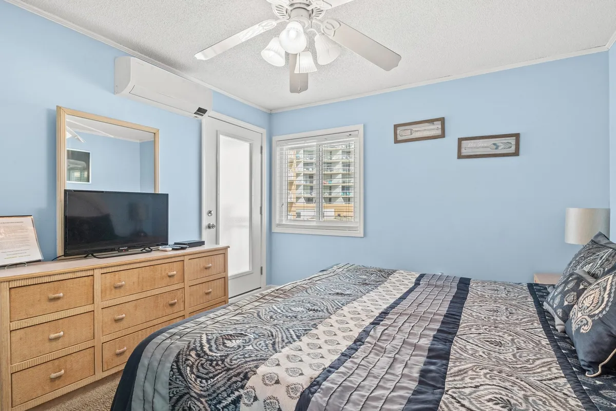 A cozy bedroom with a plush King bed, a dresser with a television, and a large window letting in natural light, creating a warm and inviting atmosphere for relaxing, watching TV, or reading. The bedding and tranquil décor enhance the sense of comfort and luxury, while the window frames a serene view.