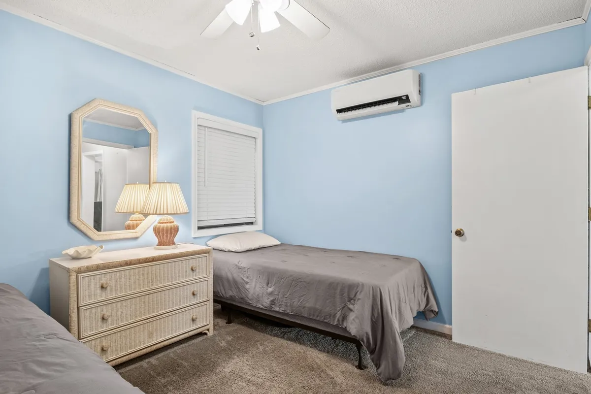 A serene bedroom featuring two twin beds with coordinated bedding, a dresser with a mirror, and a soft lamp that casts a warm, cozy glow. The space is styled for comfort, making it ideal for children or friends to share peaceful nights or quiet moments.