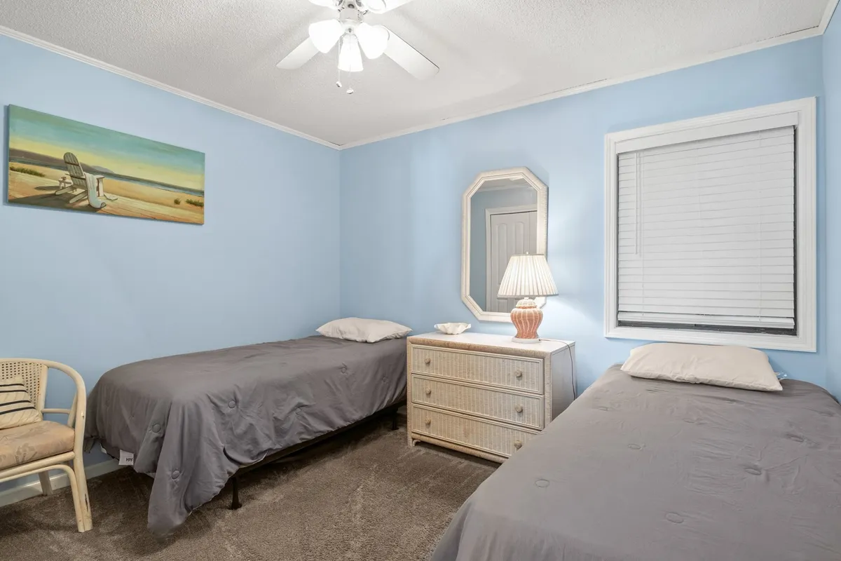 A small, functional interior featuring two twin beds, a dresser, a lamp, and a painting. The scene is cozy and relaxed, evoking the comfort and practicality that travelers—especially families—seek during extended stays.