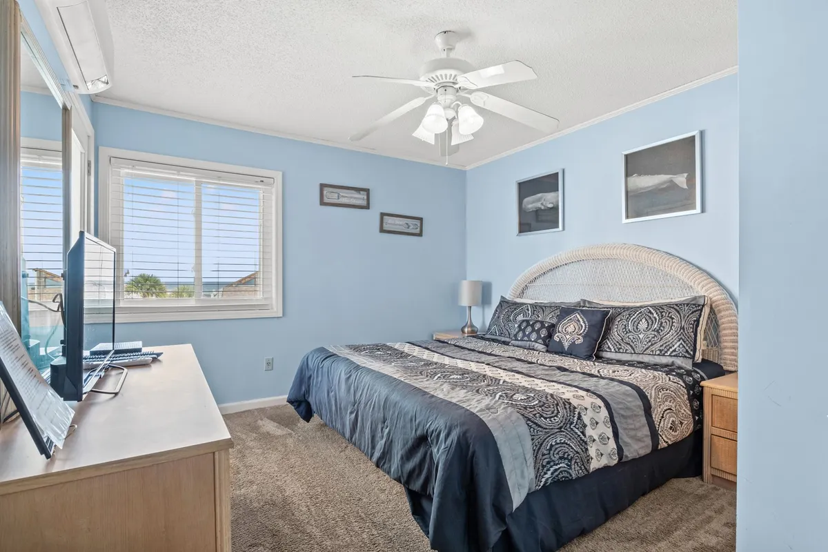 A bright, inviting bedroom scene with a bed dressed in soft, decorative bedding, a nightstand with a lamp, artwork on the wall, and ample natural light pouring through the window. The room exudes tranquility and invites guests to unwind and recharge.